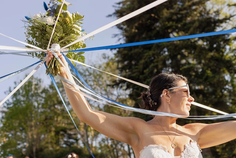 Une femme vêtue d'une robe de mariée tient son bouquet de mariage en hauteur avec des rubans.