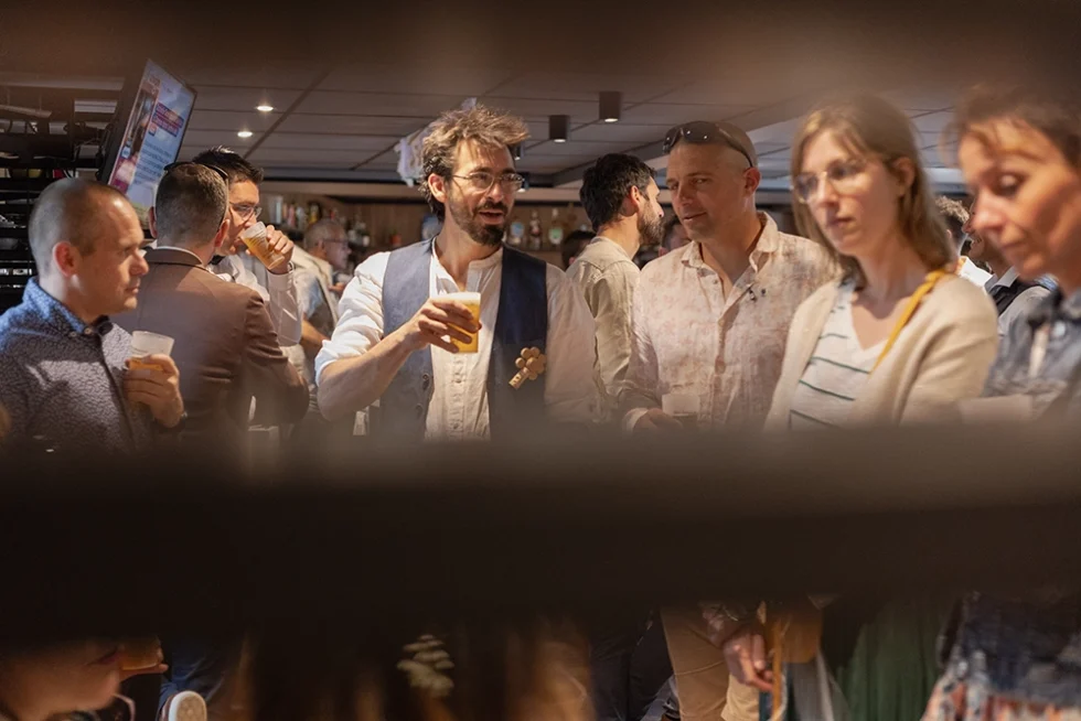 Cinq adultes, deux femmes et trois hommes, réunis autour d’un verre lors d’une fête d’anniversaire, probablement en entreprise.