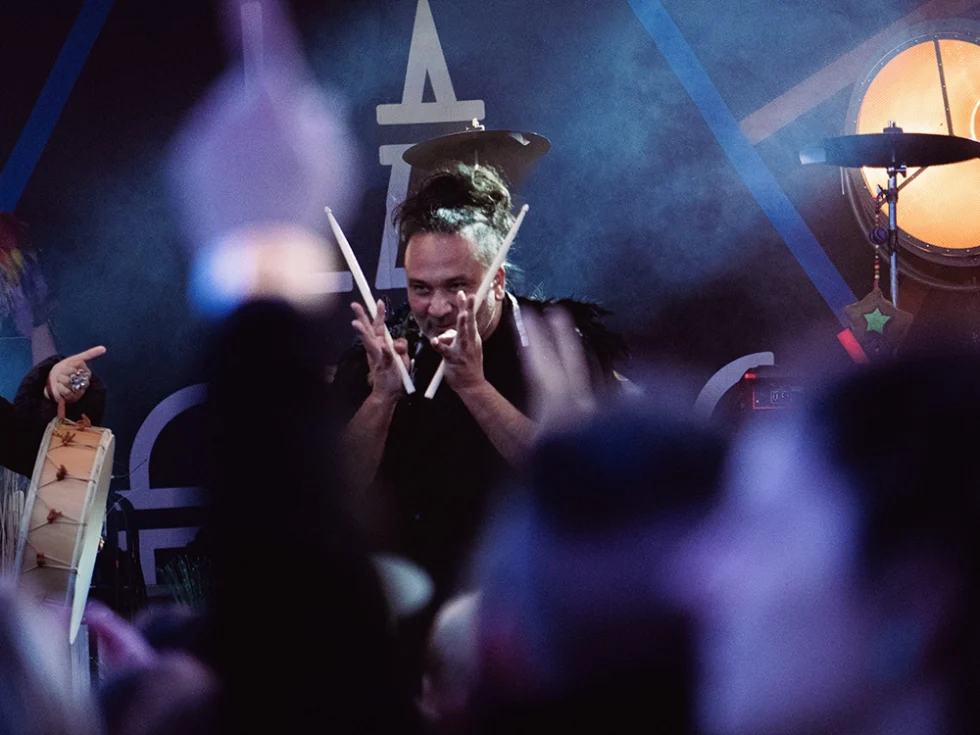 Photo d'un musicien lors d'un concert. Il est batteur et tient des baguettes en bois dans ses mains.