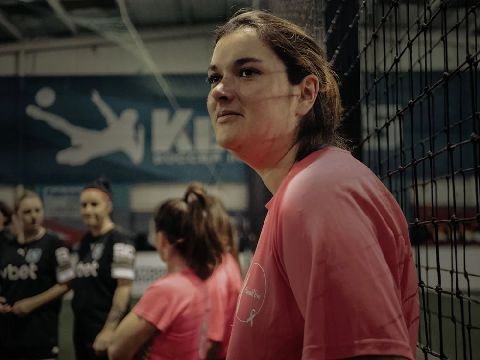 Jeune femme devant un filet lors d'un match de sport. Elle porte un tshirt rose.